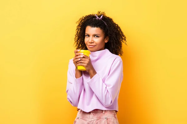 Mujer afroamericana feliz sosteniendo la taza termo en amarillo - foto de stock