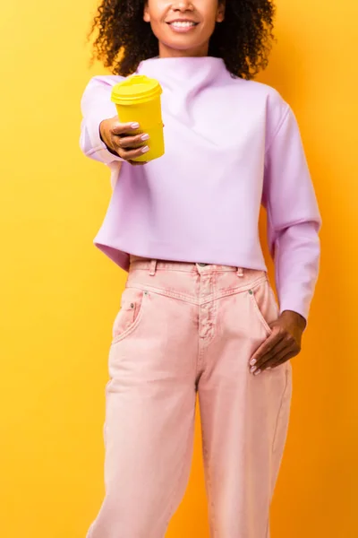 Vista recortada de la mujer afroamericana feliz sosteniendo la taza termo en amarillo - foto de stock