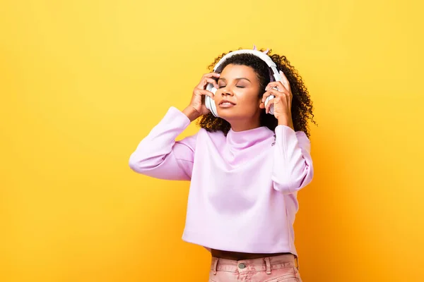 African american woman listening music in wireless headphones on yellow — Stock Photo