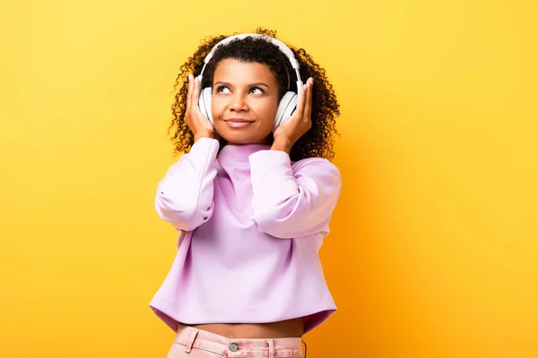 Mulher afro-americana satisfeita ouvir música em fones de ouvido em amarelo — Fotografia de Stock