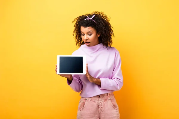 Шокована афроамериканська жінка тримає цифровий планшет з порожнім екраном на жовтому — стокове фото