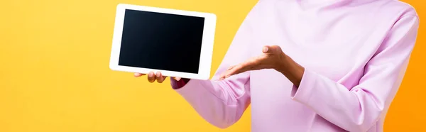 Частковий вигляд афроамериканки, що вказує рукою цифровий планшет з порожнім екраном на жовтому, банер — стокове фото