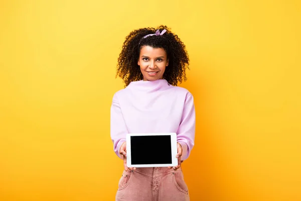 Happy african american woman holding digital tablet with blank screen on yellow — Stock Photo