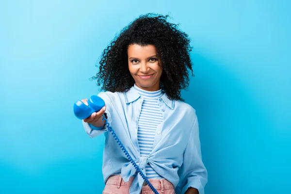 Pleased african american woman holding retro telephone on blue — Stock Photo