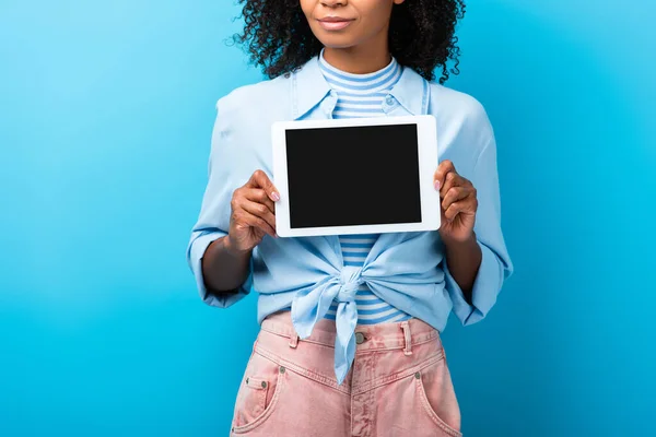 Vista recortada de la mujer afroamericana rizada sosteniendo tableta digital con pantalla en blanco en azul - foto de stock