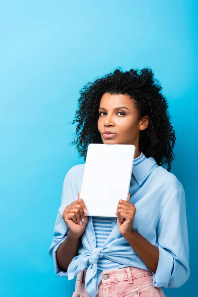 Curly african american woman holding digital tablet on blue — Stock Photo