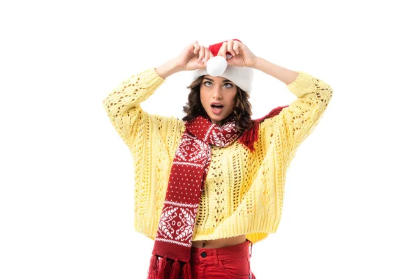 Sorpresa giovane donna in sciarpa toccante cappello di Babbo Natale isolato su bianco — Foto stock