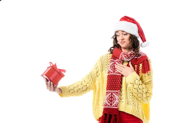 Skeptical woman in santa hat and red scarf looking at present isolated on white — Stock Photo