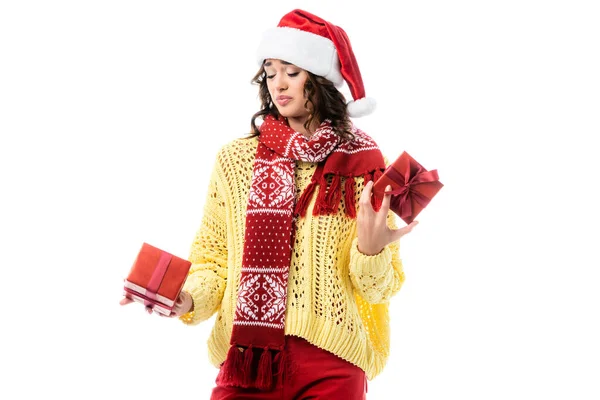 Skeptical woman in santa hat and red scarf holding presents isolated on white — Stock Photo