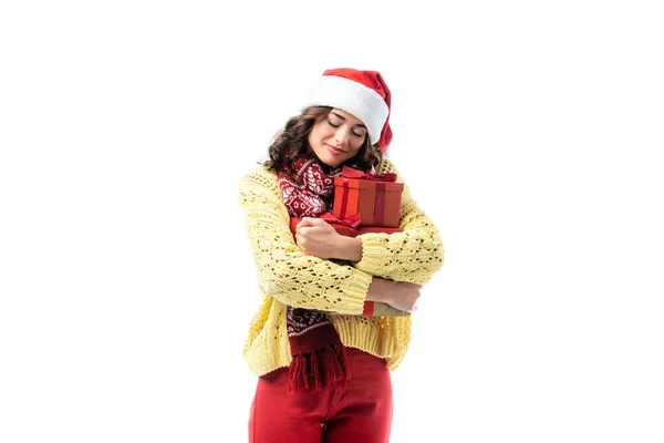 Joyful young woman in santa hat and scarf embracing gifts isolated on white — Stock Photo