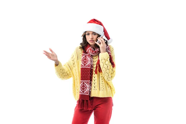 Молода жінка в капелюсі Санта і шарфі говорить на смартфоні і жестикулює ізольовано на білому — стокове фото