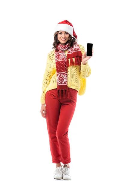 Heureuse jeune femme en santa chapeau et écharpe tenant smartphone avec écran blanc isolé sur blanc — Photo de stock