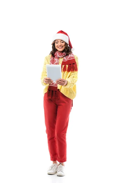 Fröhliche junge Frau mit Weihnachtsmütze und Schal, die auf ein digitales Tablet schaut, das isoliert auf weißem Grund steht — Stockfoto