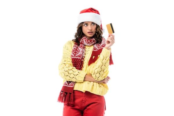 Молодая женщина в шляпе Санты и шарфе глядя на кредитную карту изолированы на белом — стоковое фото