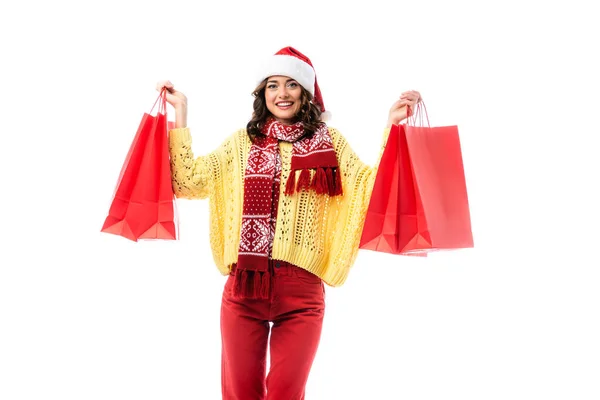 Erfreut Frau mit Weihnachtsmütze und Schal mit Ornament hält rote Einkaufstüten isoliert auf weiß — Stockfoto