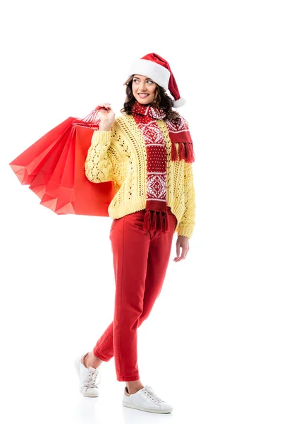 Задоволена жінка в капелюсі Санта і шарфі з орнаментом, що тримає сумки для покупок ізольовані на білому — стокове фото