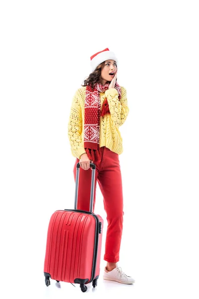 Schockierte junge Frau mit Weihnachtsmütze und Schal mit Ornament steht mit Reisetasche isoliert auf weiß — Stockfoto