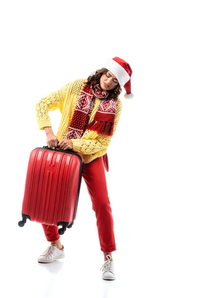 Giovane donna in cappello di Babbo Natale e sciarpa con ornamento che trasporta borsa da viaggio pesante isolata su bianco — Foto stock