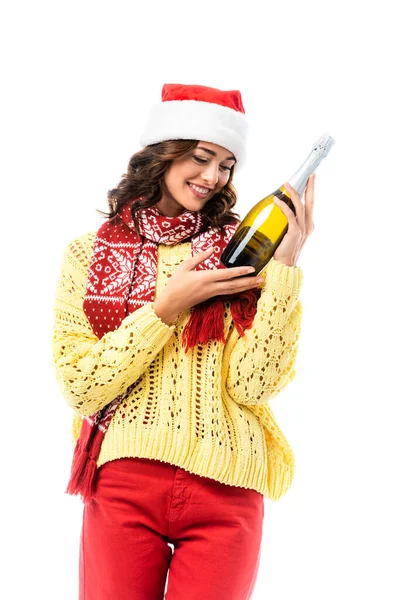 Freudige junge Frau mit Weihnachtsmütze und Schal mit Ornament, die auf eine Champagnerflasche auf weißem Grund blickt — Stockfoto