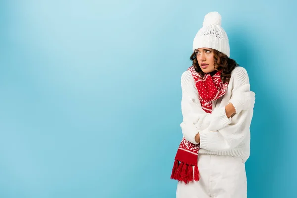 Freezing young woman in winter outfit embracing herself on blue — Stock Photo