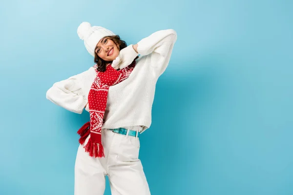 Pleased young woman in white winter outfit, warm scarf, gloves and hat on blue — Stock Photo