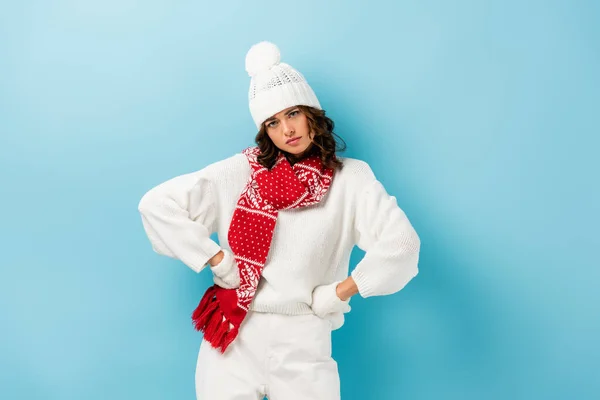 Serious young woman in white winter outfit standing with hands on hips on blue — Stock Photo