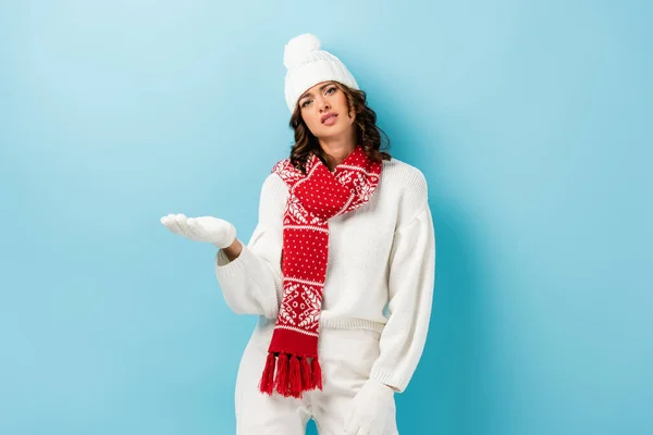 Unzufriedene junge Frau im weißen Winteroutfit zeigt mit der Hand auf blau — Stockfoto