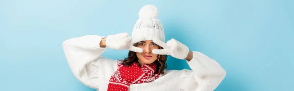 Panoramic crop of young woman in white winter outfit showing peace sign on blue — Stock Photo