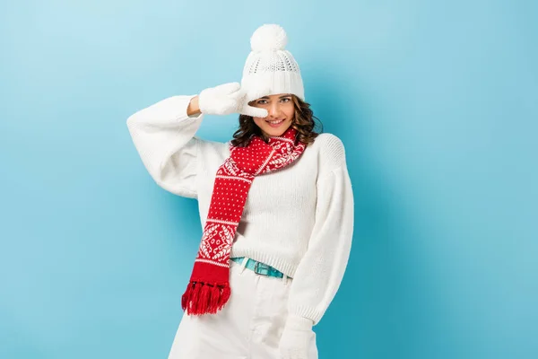 Zufriedene junge Frau im weißen Winteroutfit mit Friedenszeichen auf blauem Grund — Stockfoto