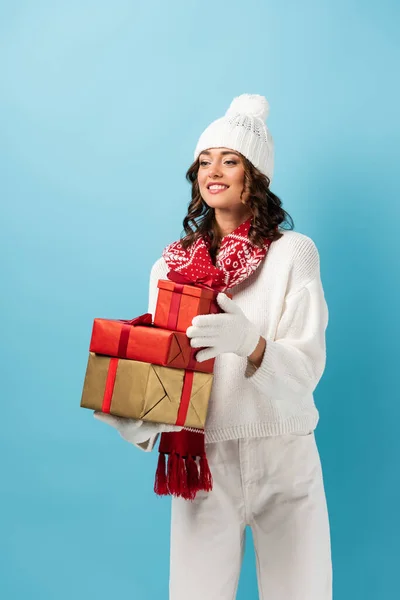 Радісна жінка в зимовому вбранні тримає подарунки на синьому — стокове фото
