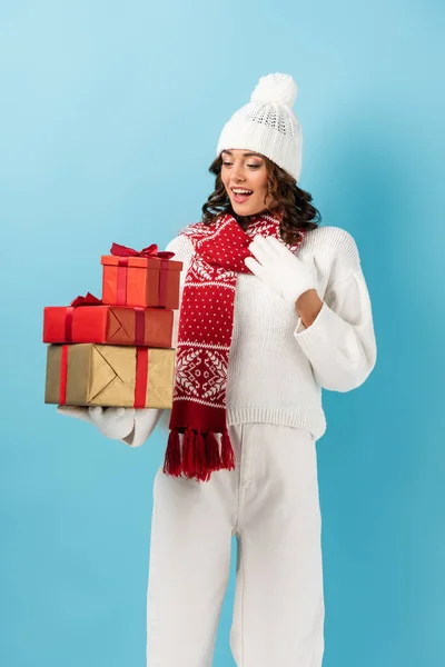 Excited and brunette woman in winter outfit holding presents on blue — Stock Photo