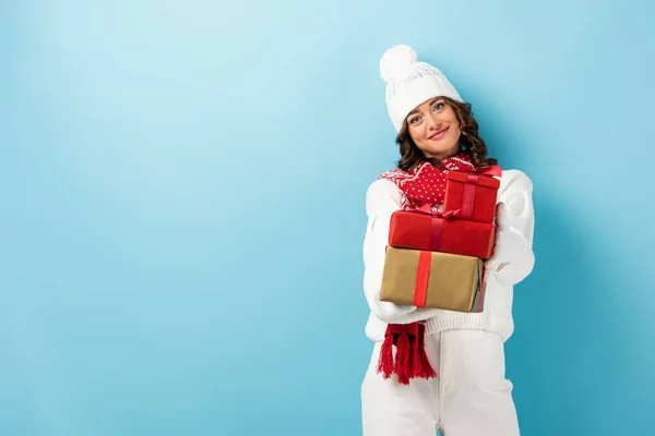 Young joyful woman in winter outfit holding presents on blue — Stock Photo