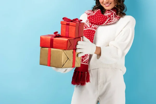 Abgeschnittene Ansicht einer glücklichen Frau im Winteroutfit mit Geschenken auf blauem Grund — Stockfoto