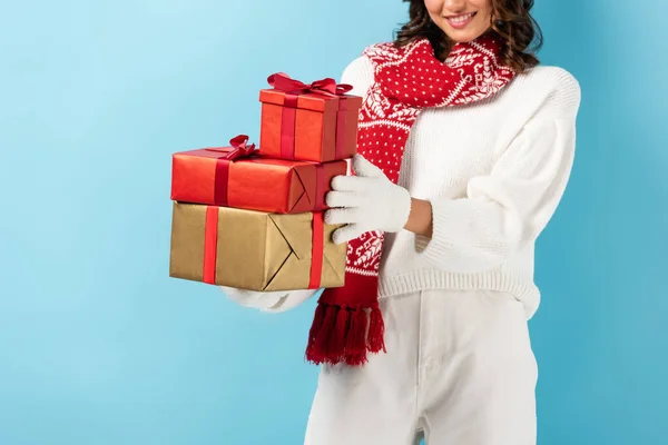 Cropped view of happy woman in winter outfit holding presents on blue — Stock Photo