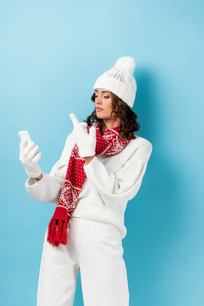 Young woman in white winter outfit showing middle finger to smartphone on blue — Stock Photo
