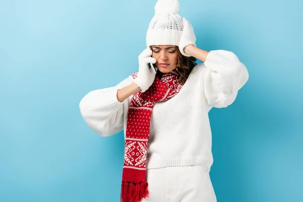 Upset young woman in white winter outfit talking on smartphone on blue — Stock Photo
