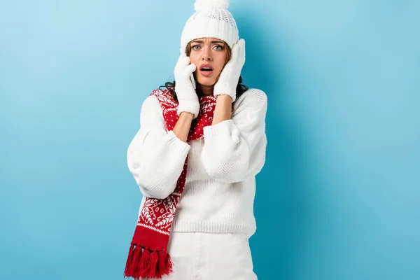 Sad young woman in white winter outfit talking on smartphone on blue — Stock Photo