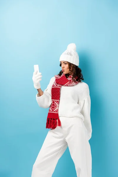 Jeune femme au visage de canard, en tenue d'hiver blanche prenant selfie sur bleu — Photo de stock