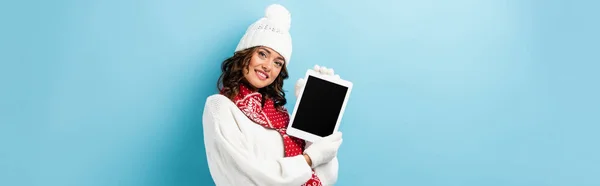 Récolte panoramique de jeune femme heureuse en tenue d'hiver tenant tablette numérique avec écran blanc sur bleu — Photo de stock