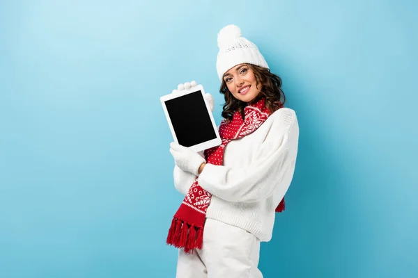 Gioiosa giovane donna in abito invernale con tablet digitale con schermo bianco su blu — Foto stock