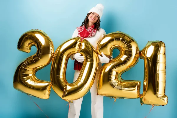 Happy woman in winter outfit holding balloons with 2021 numbers on blue — Stock Photo