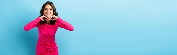 Panoramic concept of pleased woman in pink dress looking at camera on blue — Stock Photo