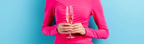 Panoramic crop of young woman holding glass of champagne on blue — Stock Photo