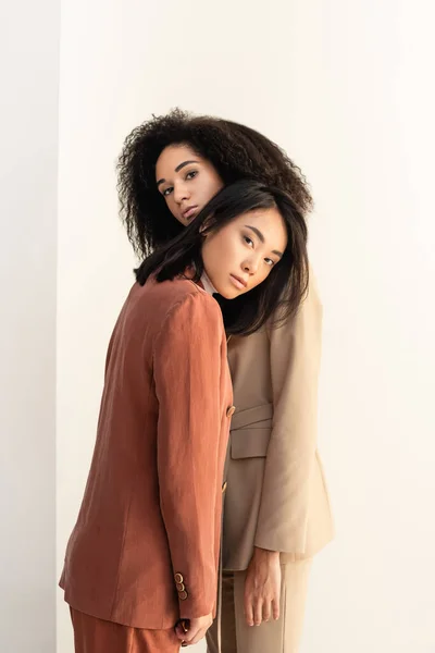 Africano americano y asiático mujeres en trajes posando en blanco - foto de stock
