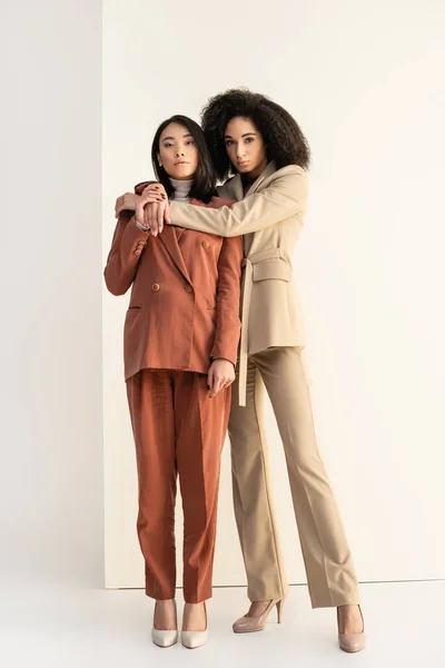 Full length of african american and asian women in suits posing on white — Stock Photo