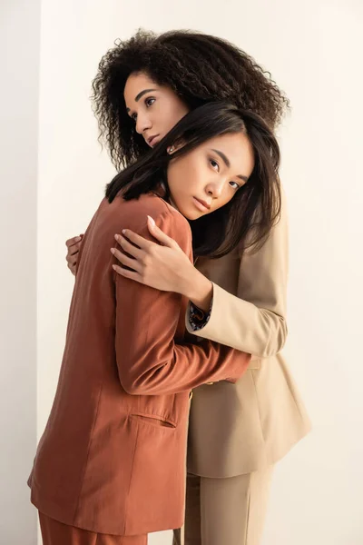 African american and asian women in suits hugging on white — Stock Photo