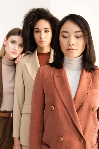 Asiatique femme en costume debout près multiculturel amis sur blanc et flou fond — Photo de stock