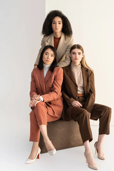 Jóvenes mujeres multiculturales en trajes elegantes mirando a la cámara en blanco - foto de stock