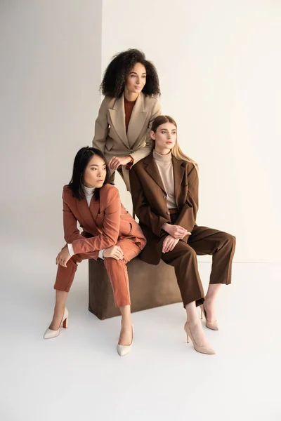 Mujeres jóvenes multiculturales en trajes elegantes mirando hacia otro lado en blanco - foto de stock