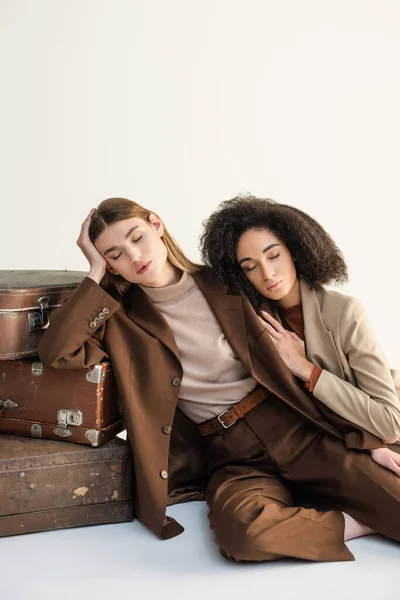 Young model and african american woman with closed eyes posing near suitcases isolated on white — Stock Photo